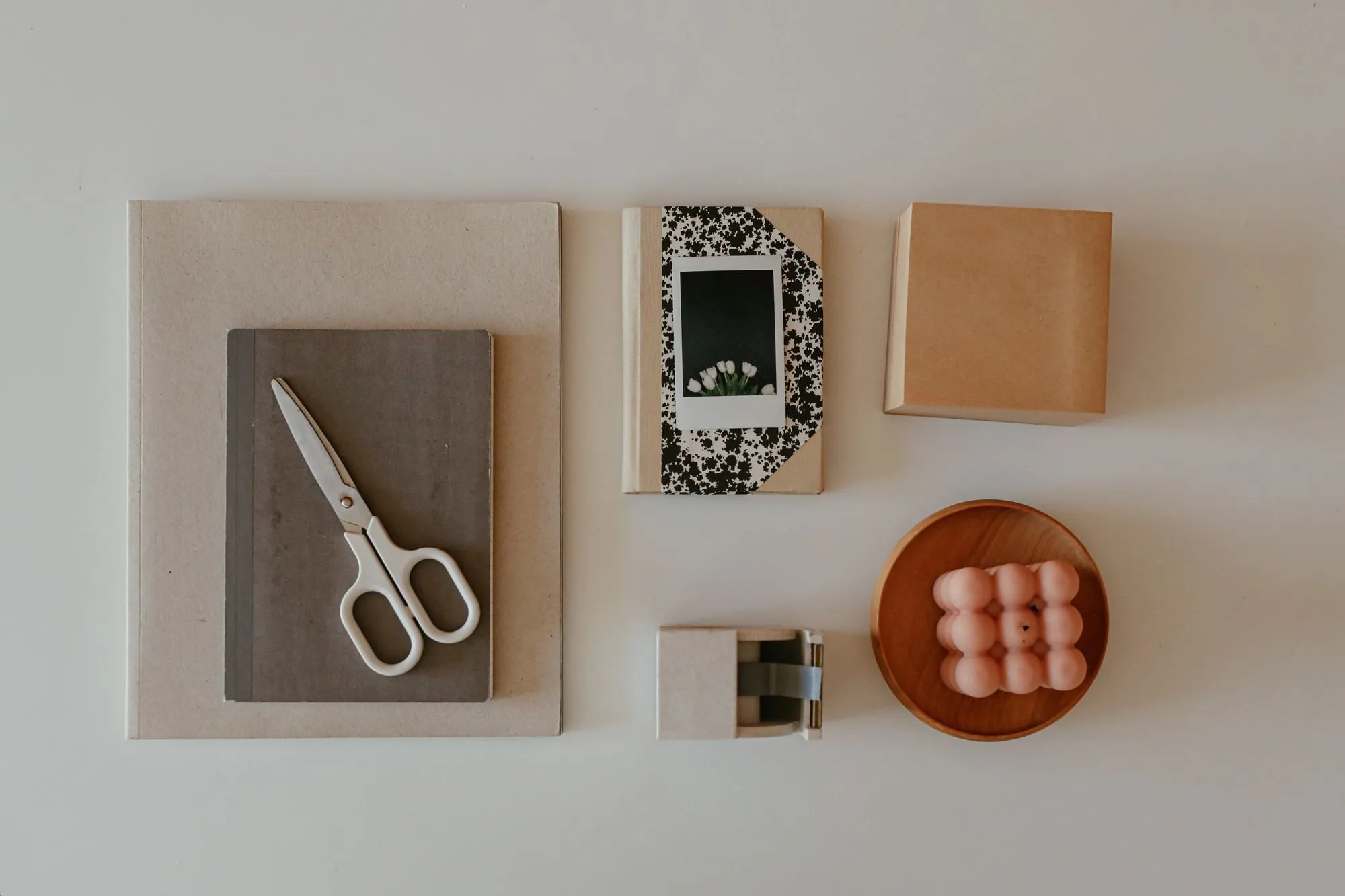 Notebooks, a kraft box, scissors and a candle laid out on a pale surface