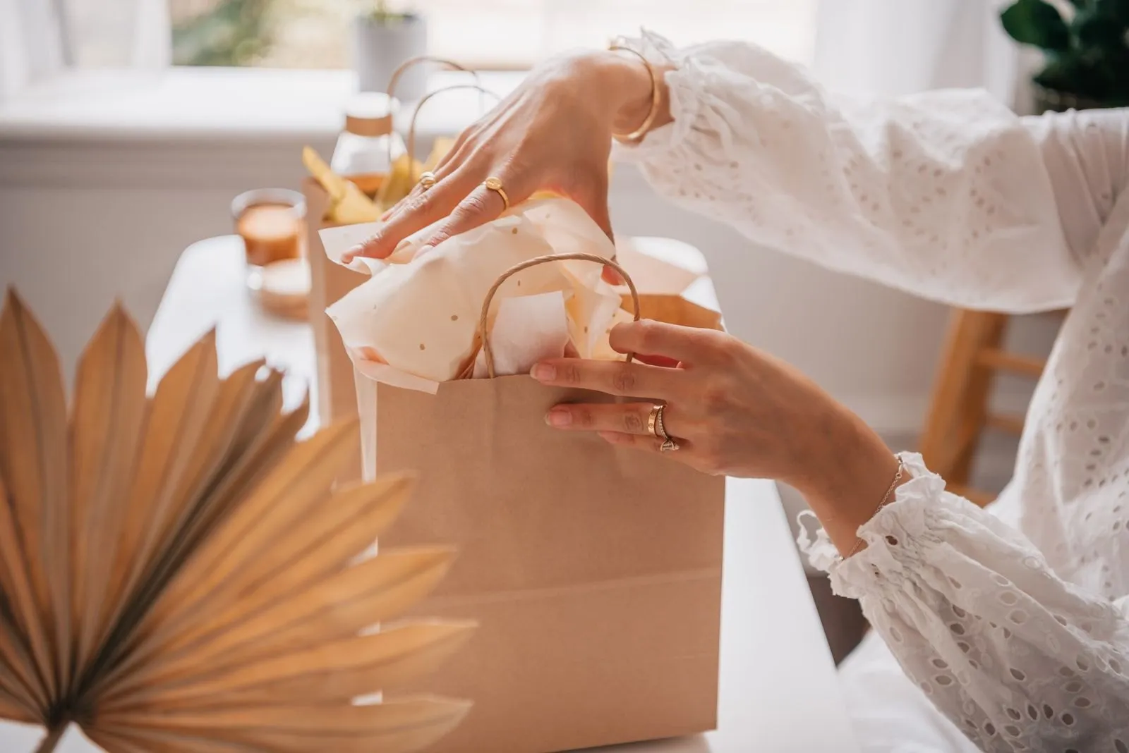 Tissue paper being tucked into a kraft gift bag on a white table